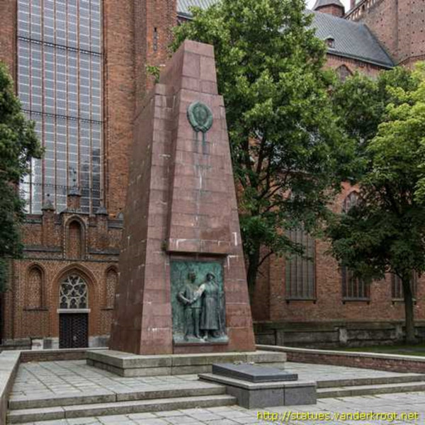 Obelisk from red granite with a relief on which a Red Army soldier and a civilian shake hands and at the top the coat of arms of the Soviet Union.